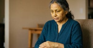 Older woman with yellowish skin tone sitting indoors looking fatigued