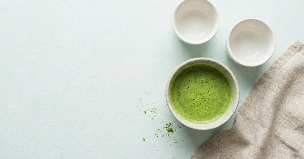 A bowl of green matcha tea with two white cups