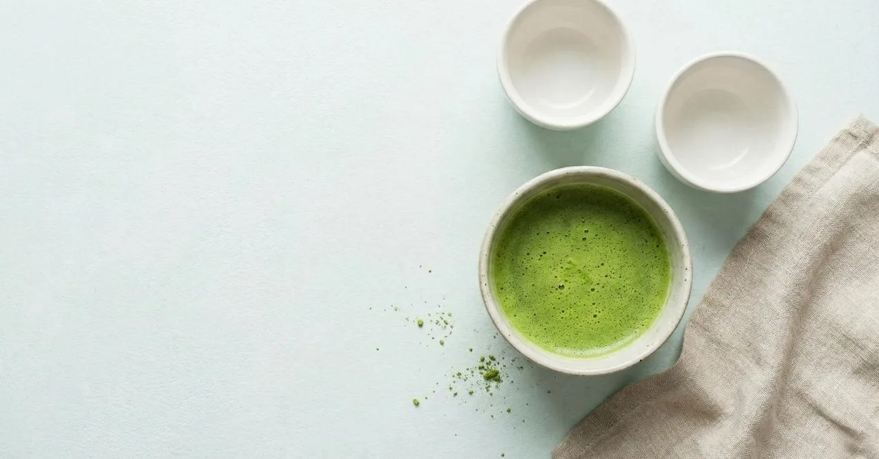A bowl of green matcha tea with two white cups