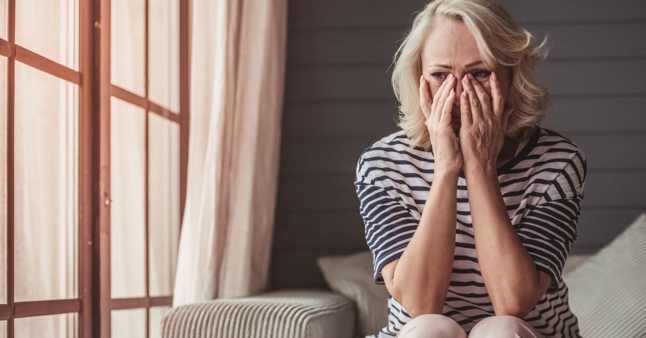 Worried woman sitting by a window with her hands covering her face