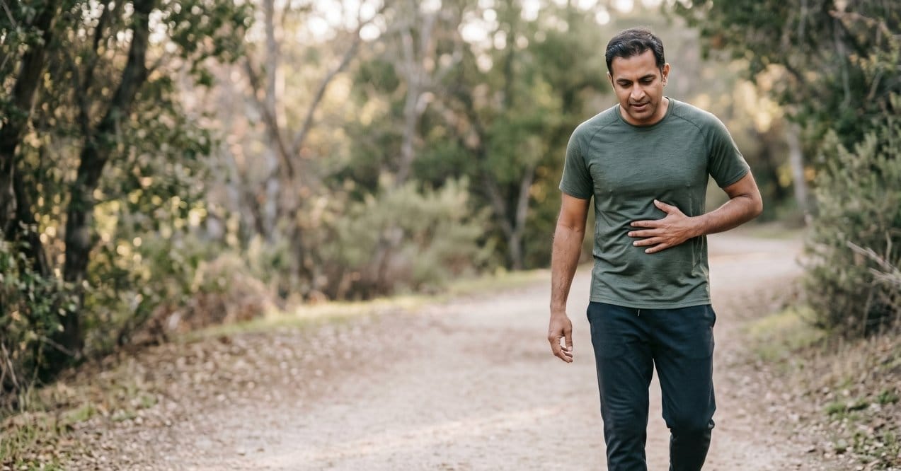 Man walking outdoors while holding his upper abdomen, illustrating discomfort in the liver area during running